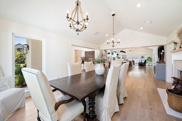 dining space featuring visible vents, light wood-style floors, lofted ceiling, a brick fireplace, and a notable chandelier