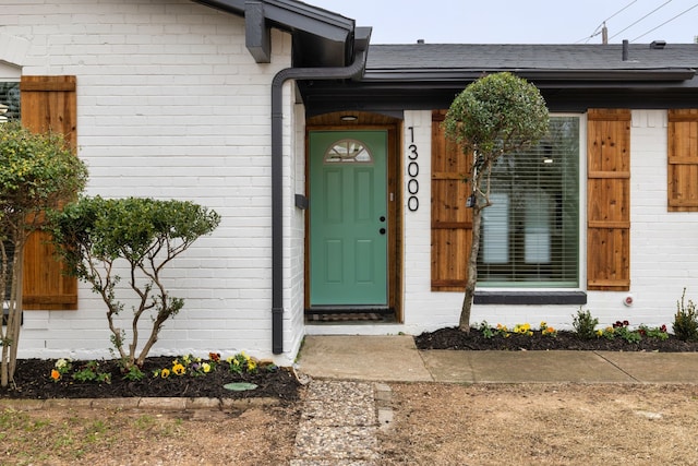 doorway to property featuring a shingled roof and brick siding