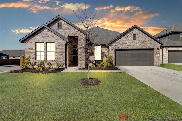 french provincial home featuring brick siding, roof with shingles, a garage, driveway, and a front lawn