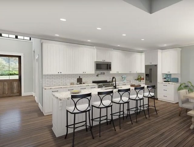 kitchen with dark wood-type flooring, a kitchen breakfast bar, white cabinets, appliances with stainless steel finishes, and a center island with sink