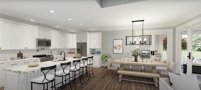 kitchen with a sink, white cabinets, hanging light fixtures, appliances with stainless steel finishes, and light stone countertops