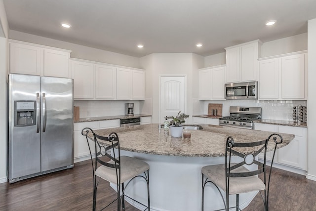 kitchen with appliances with stainless steel finishes, white cabinetry, a center island with sink, and a breakfast bar area