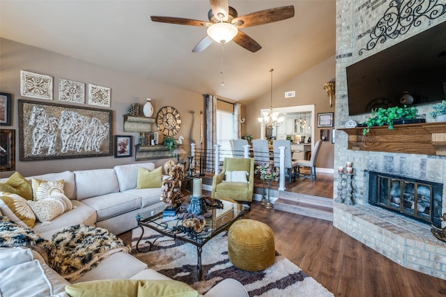 living room with visible vents, dark wood finished floors, lofted ceiling, a fireplace, and ceiling fan with notable chandelier