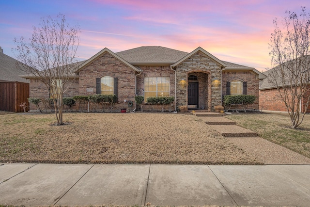 french country inspired facade with roof with shingles, brick siding, and a lawn