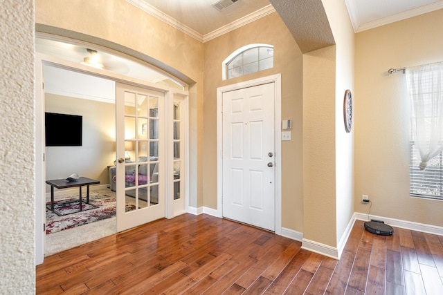 foyer entrance with baseboards, wood finished floors, visible vents, and crown molding