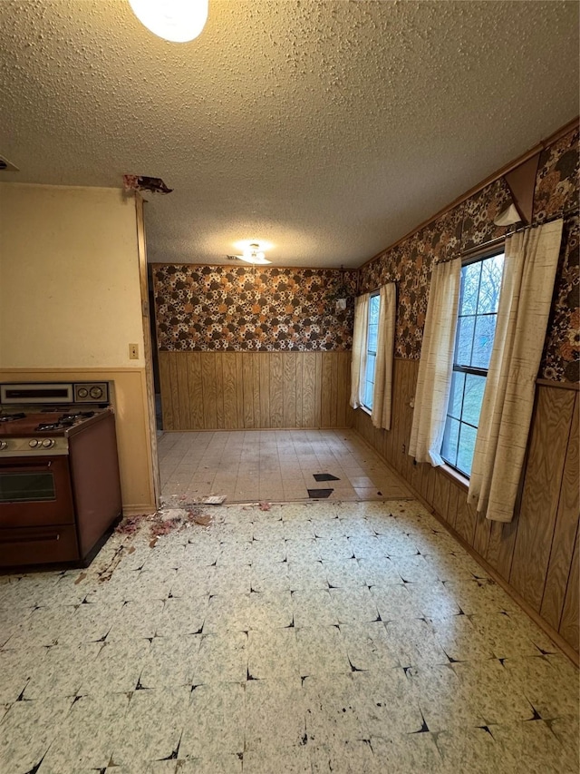 unfurnished room with a wainscoted wall, a textured ceiling, light floors, and wood walls