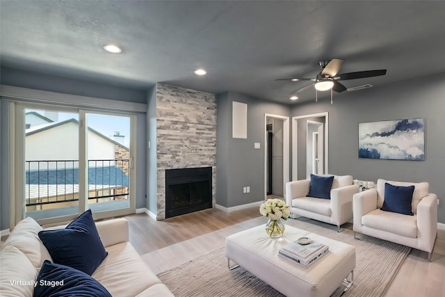 living room with a stone fireplace, light wood-style flooring, recessed lighting, a water view, and baseboards