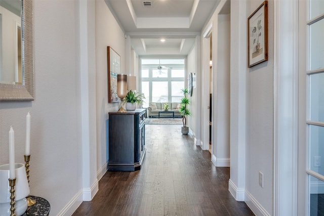 hallway featuring a tray ceiling, dark wood-type flooring, visible vents, and baseboards