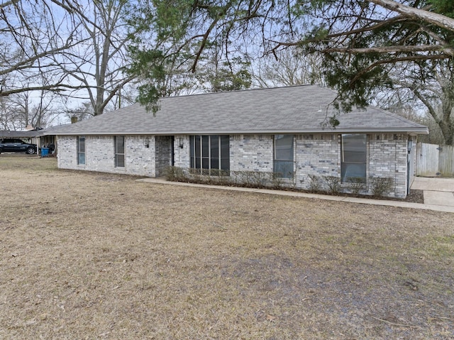 ranch-style house featuring a shingled roof, a front yard, and brick siding