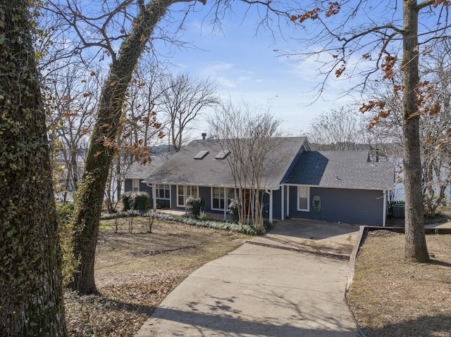 view of front facade featuring concrete driveway, a shingled roof, and central air condition unit