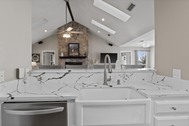 kitchen with visible vents, lofted ceiling with skylight, a sink, light stone countertops, and dishwasher