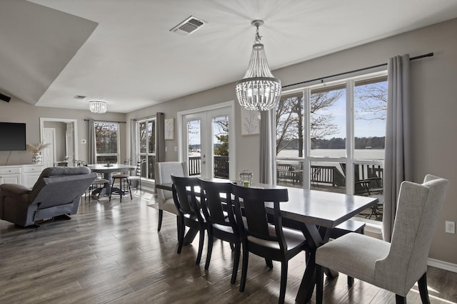 dining area featuring dark wood-style floors, a water view, a notable chandelier, and visible vents