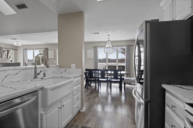 kitchen with white cabinets, light stone counters, hanging light fixtures, stainless steel appliances, and a notable chandelier