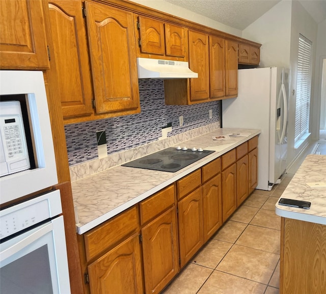 kitchen featuring brown cabinets, light tile patterned floors, light countertops, white appliances, and under cabinet range hood