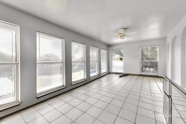 unfurnished room with light tile patterned floors, ceiling fan, and arched walkways