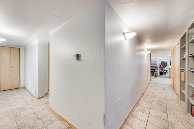 hall with light tile patterned flooring, visible vents, and baseboards