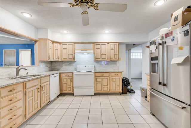 kitchen featuring white appliances, light stone counters, light brown cabinetry, under cabinet range hood, and a sink