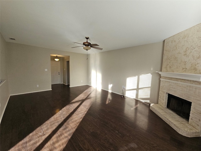 unfurnished living room featuring wood finished floors, visible vents, baseboards, a ceiling fan, and a brick fireplace