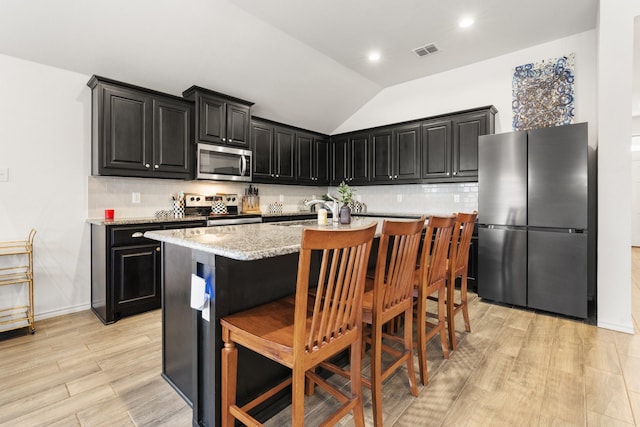 kitchen with stainless steel appliances, visible vents, an island with sink, dark cabinetry, and a kitchen breakfast bar