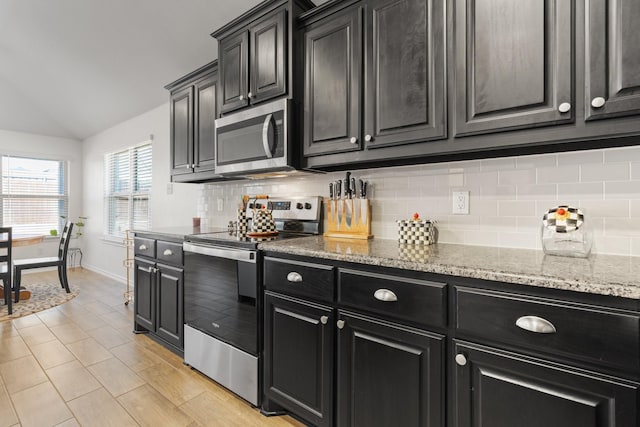 kitchen featuring stainless steel appliances, dark cabinetry, backsplash, and light stone counters