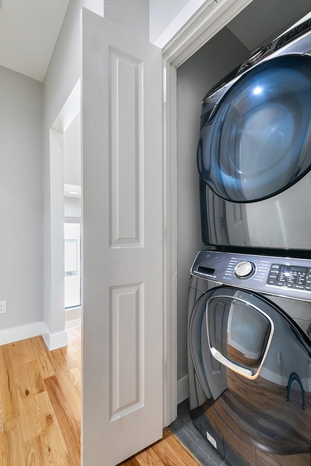 laundry room with stacked washer and dryer, laundry area, baseboards, and light wood finished floors