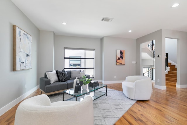 living room featuring recessed lighting, visible vents, light wood-type flooring, baseboards, and stairs