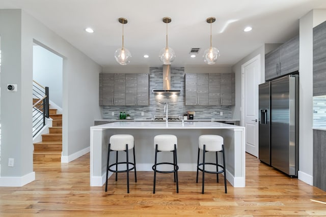 kitchen featuring light countertops, gray cabinets, wall chimney exhaust hood, stainless steel fridge, and decorative light fixtures