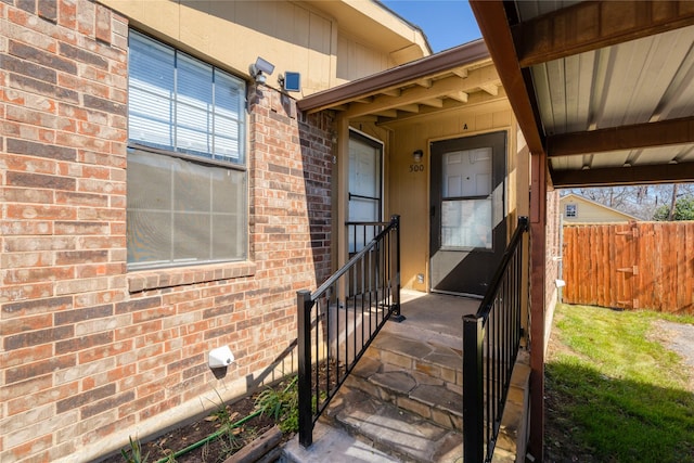 doorway to property featuring fence and brick siding