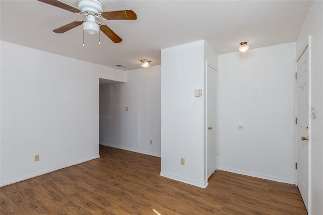 empty room with dark wood-type flooring, visible vents, ceiling fan, and baseboards