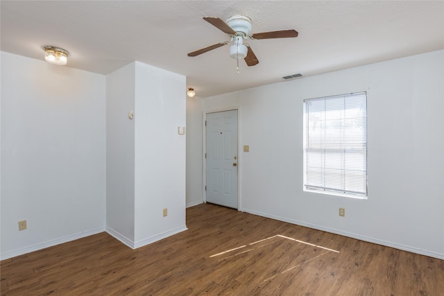 spare room featuring baseboards, visible vents, ceiling fan, and dark wood-type flooring