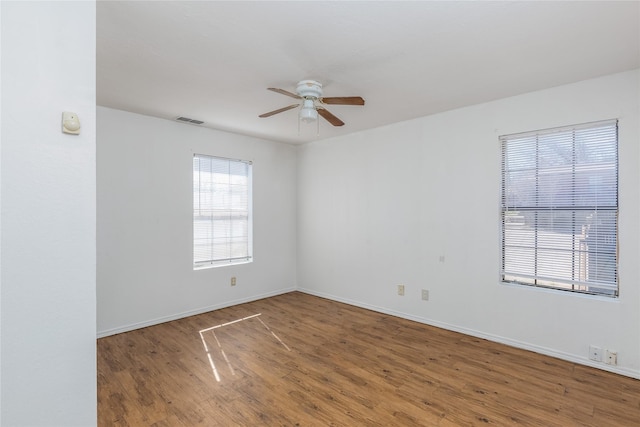 empty room featuring baseboards, ceiling fan, visible vents, and wood finished floors