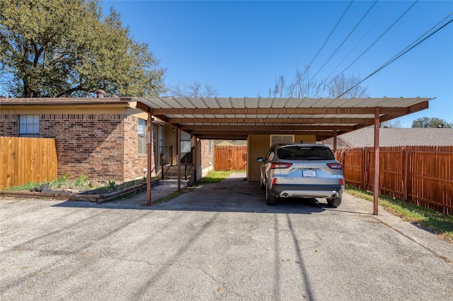 view of vehicle parking with aphalt driveway, fence, and a detached carport