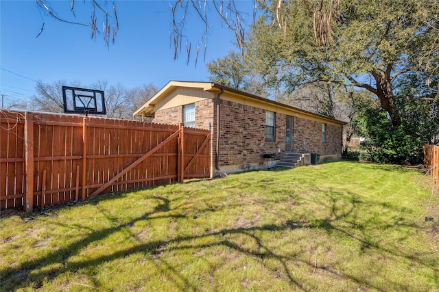 view of side of home featuring a yard, brick siding, central AC unit, and fence