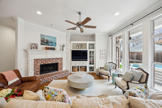 living area featuring a ceiling fan, ornamental molding, wood finished floors, a brick fireplace, and recessed lighting