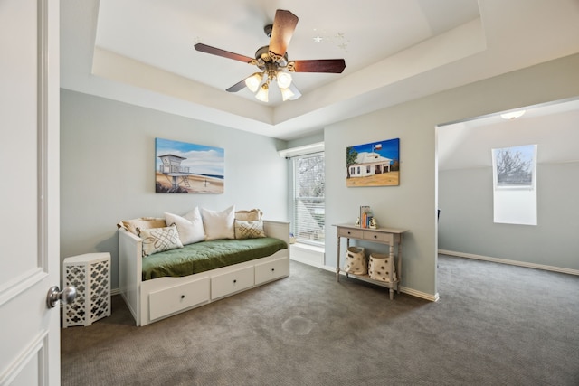 bedroom with ceiling fan, a tray ceiling, dark carpet, and baseboards