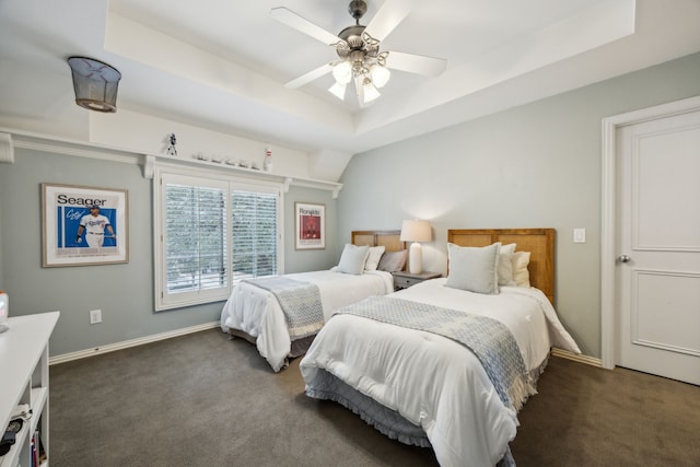 bedroom featuring a ceiling fan, a tray ceiling, dark carpet, and baseboards