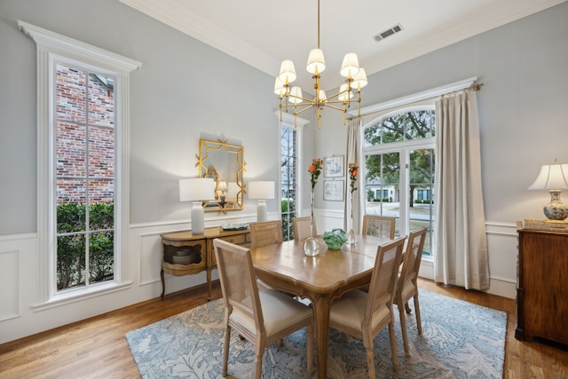 dining room featuring light wood finished floors, visible vents, wainscoting, crown molding, and a chandelier