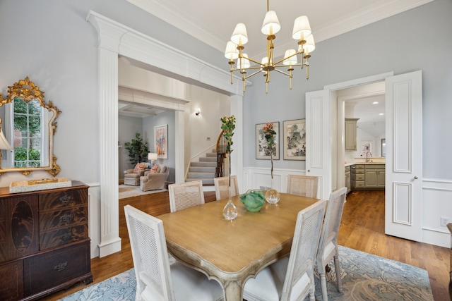 dining space featuring dark wood finished floors, crown molding, a decorative wall, an inviting chandelier, and wainscoting