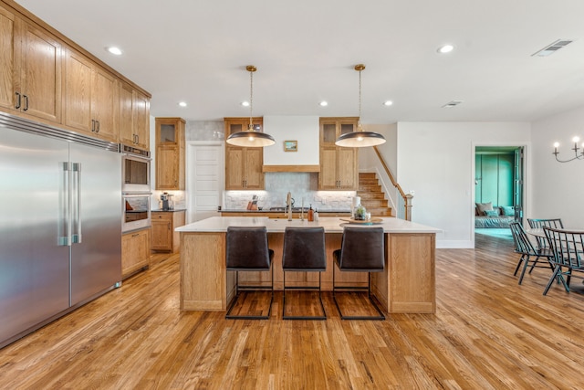 kitchen featuring light countertops, appliances with stainless steel finishes, an island with sink, and pendant lighting