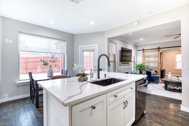 kitchen with a barn door, a kitchen island with sink, a sink, white cabinetry, and open floor plan