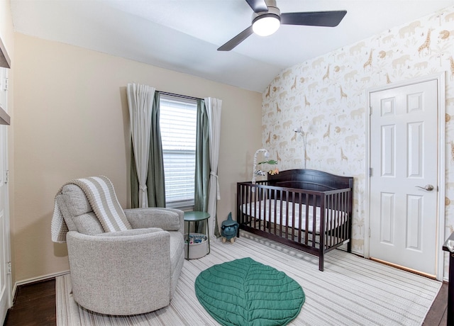 bedroom featuring a crib, wallpapered walls, lofted ceiling, wood finished floors, and a fireplace