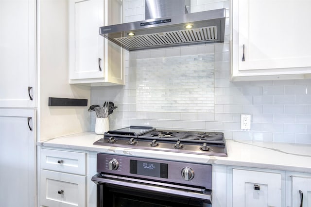 kitchen featuring light stone countertops, stainless steel appliances, white cabinetry, backsplash, and exhaust hood