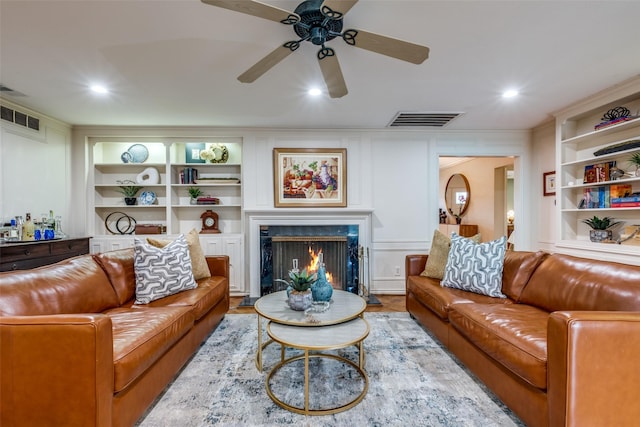 living area featuring light wood-type flooring, built in shelves, a fireplace, and visible vents