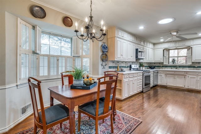 dining room with a wainscoted wall, visible vents, wood finished floors, and ceiling fan with notable chandelier