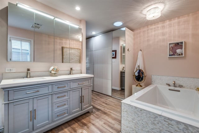 full bath featuring a garden tub, double vanity, wood finished floors, and a sink