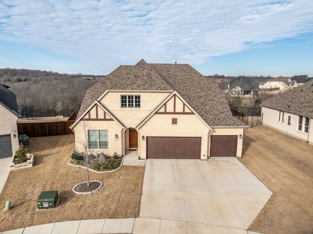 tudor house with concrete driveway, a shingled roof, an attached garage, and brick siding