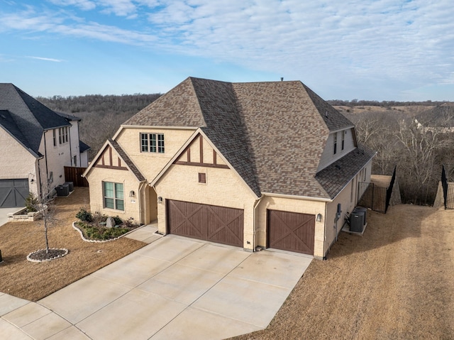 tudor-style house featuring a garage, central AC, driveway, roof with shingles, and a front lawn