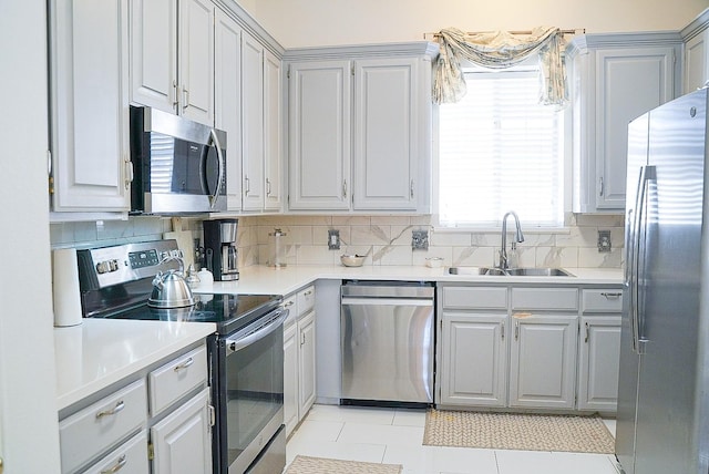 kitchen with gray cabinetry, a sink, light countertops, appliances with stainless steel finishes, and decorative backsplash