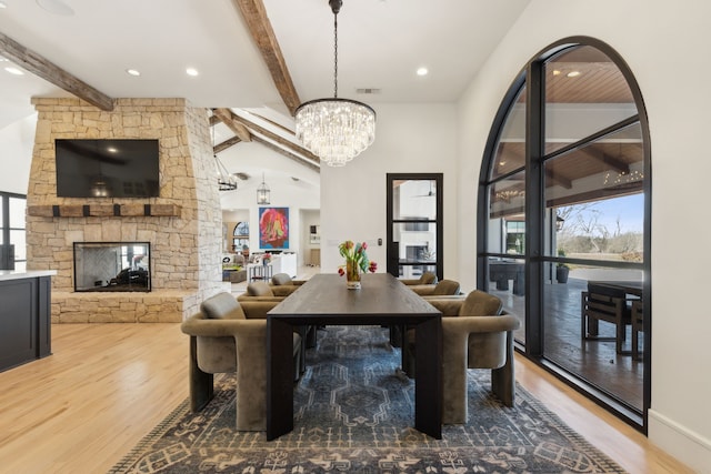 dining room featuring wood finished floors, a chandelier, a wealth of natural light, and a stone fireplace