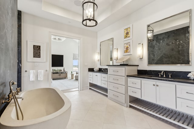 ensuite bathroom with connected bathroom, a sink, tile patterned floors, double vanity, and a tray ceiling